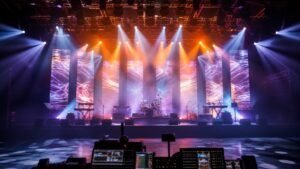 Empty concert stage with instruments, haze, projection panels, lighting rig, stage monitors, and distant control booth