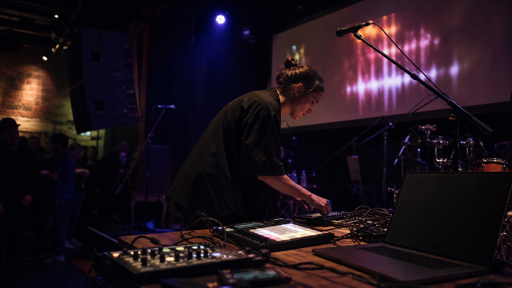 Contemporary live music stage with performers' instruments, controllers, microphones, monitors, lights, and blank screens