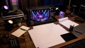 Production planning room with blank blueprint sheets, miniature stage, lighting fixtures, cables, keyboard, guitar, blank tablet, and acoustic panels