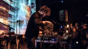 Experimental performer preparing AI-assisted music equipment on a small live stage